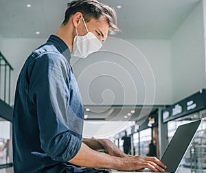 Man in a protective mask works on a laptop in a shopping center building.