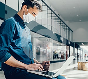 Man in a protective mask works on a laptop in a shopping center building.