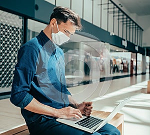 man in a protective mask works on a laptop in a shopping center building.