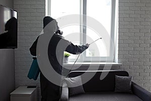 A man in a protective suit cleans the window with a chemical agent, protecting the house from coronavirus