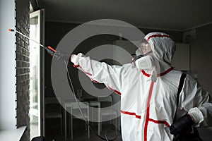 A man in a protective suit cleans the window with a chemical agent, protecting the house from coronavirus