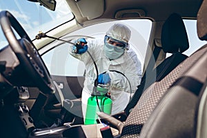 Man in protective suit with mask disinfecting inside car.