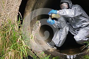 A man in a protective suit and mask in a large sewer took a sample of water for analysis