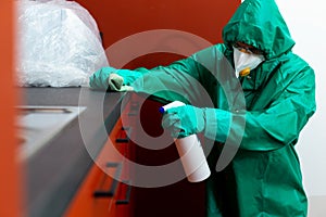 Man in protective suit spraying chemicals on kitchen cabinetry