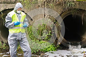 A man in a protective suit takes soil samples into a Petri dish from the sewage treatment plant
