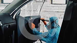 A man in a protective suit vacuums the door of a car from the inside.