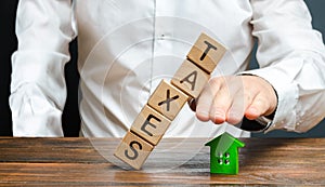 A man protects his hand with a figurine of a house from a falling tower of cubes with the word taxes. Heavy tax burden, protecting