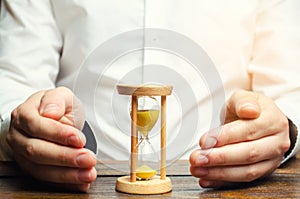 Man protects the hourglass. Concept of saving time and money. Time management. Planning work. Reduced cost and bureaucratic burden photo