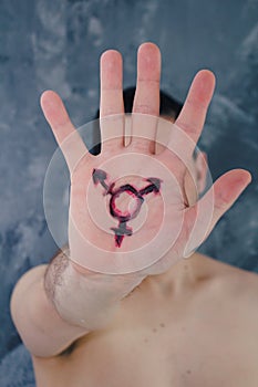 A man proudly holds his palm in front of his face. It has a symbol for the third sex on the palm.