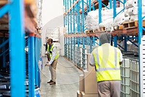 Man pulling pallet jack while supervisors work in aisle in warehouse.