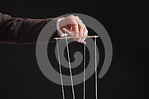 Man pulling strings of puppet on black background, closeup