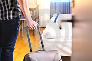 Man pulling suitcase and entering hotel room.