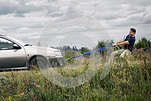 Man pulls his broken down car along a country road using a tow rope