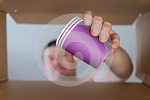 A man pulls lilac cups out of a cardboard moving box. A set of disposable paper beverage glasses. Bottom view. Inside view. Close-