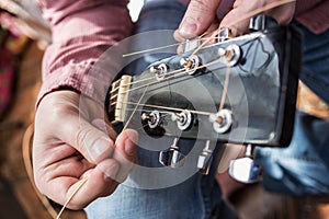 Man pulls new guitar strings acoustic guitar in closeup