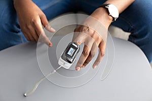 Man with pulse oximeter on hand measuring oxygen saturation indoor