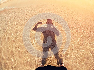 Man pumped up muscles makes selfie silhouette shadows from sun on golden sand and sea. Concept preparation for summer