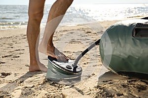 Man pumping inflatable rubber fishing boat at sandy beach on sunny day, closeup