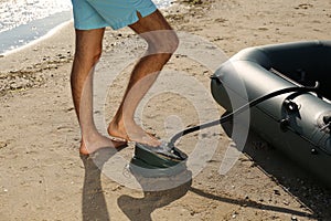 Man pumping inflatable rubber fishing boat at sandy beach on sunny day, closeup