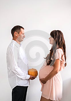 Man with pumpkin opposite a pregnant woman.