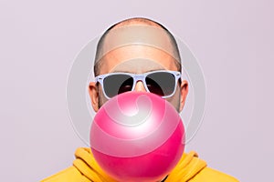 Man with purple sunglasses blowing pink chewing gum and facing the camera