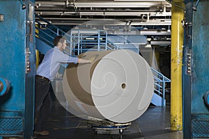 Man Pushing Huge Roll Of Paper In Factory