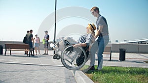 A man is pushing a wheelchair. A man helps a woman in a wheelchair