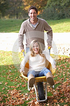 Man pushing wife through autumn leaves