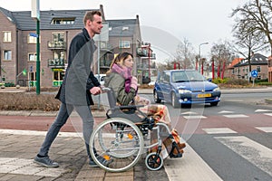 Man pushing a woman in a wheelchair at a zebra crosssing