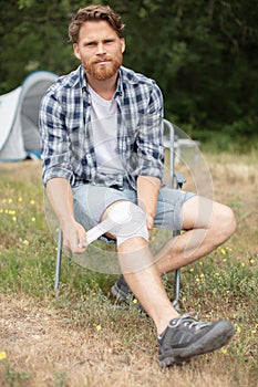 man put bandage on hurt knee in camping