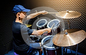 Man put black t-shirt to playing the drum set with wooden drumsticks in music room