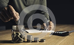 A man put coins in a glass jar and took notes to save money on a wooden table