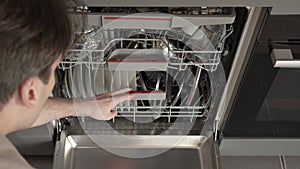 The man put the dirty dishes in the dishwasher and starts the washing cycle.