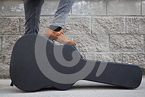 Man put his foot on a hard guitar case. hard case for electric guitar. Man dressed in jeans holding guitar case against wall. guy