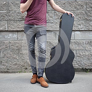 Man put his foot on a hard guitar case. hard case for electric guitar. Man dressed in jeans holding guitar case against wall. guy