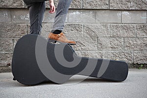 Man put his foot on a hard guitar case. hard case for electric guitar. Man dressed in jeans holding guitar case against wall. guy