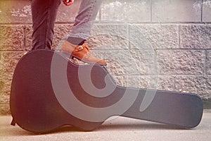 Man put his foot on a hard guitar case. hard case for electric guitar. Man dressed in jeans holding guitar case against wall. guy