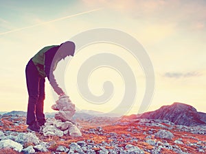 Man put the last stone intopeak of pyramid. Balanced stone pyramid on mountain summit.