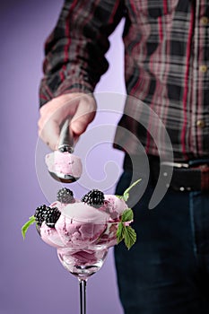 Man puts blackberry ice cream in a sundae cup