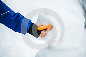 Man puts a carrot the a snowman figure, bodypart hand and arm