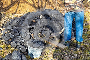 A man puts coal into a bucket with a shovel. Heating a house in the countryside