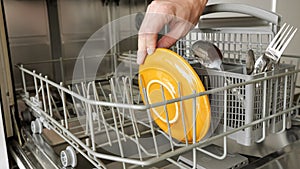 Man puts a dirty plates and cutlery in dishwasher