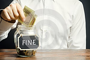 A man puts dollars in a glass jar with the word Fine. Saving money and paying a fine. Punishment for a crime and offense.