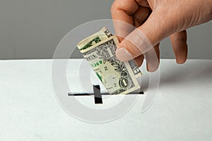 Man puts donation in his hand with dollar in slot in the form of Christian cross