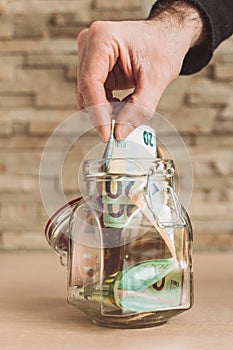 A man puts Euro banknotes in a glass jar - replenishment of family budget