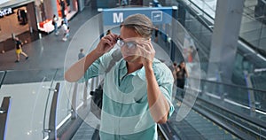 Man puts glasses descending escalator. Escalator descent marks journey. Glasses signify start journey. Escalator