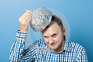 Man puts on a helmet made of aluminum foil with pleased face.. Protects from reading think