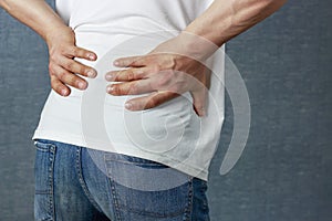A man puts his hand on a sore back, close-up rear view photo