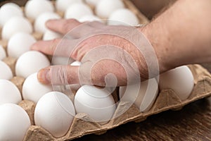 A man puts his hand on top of a cardboard tray of chicken eggs. Open recycled tray