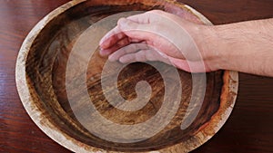 Man puts his hand in a wooden bowl of water and grabs the water in his fists